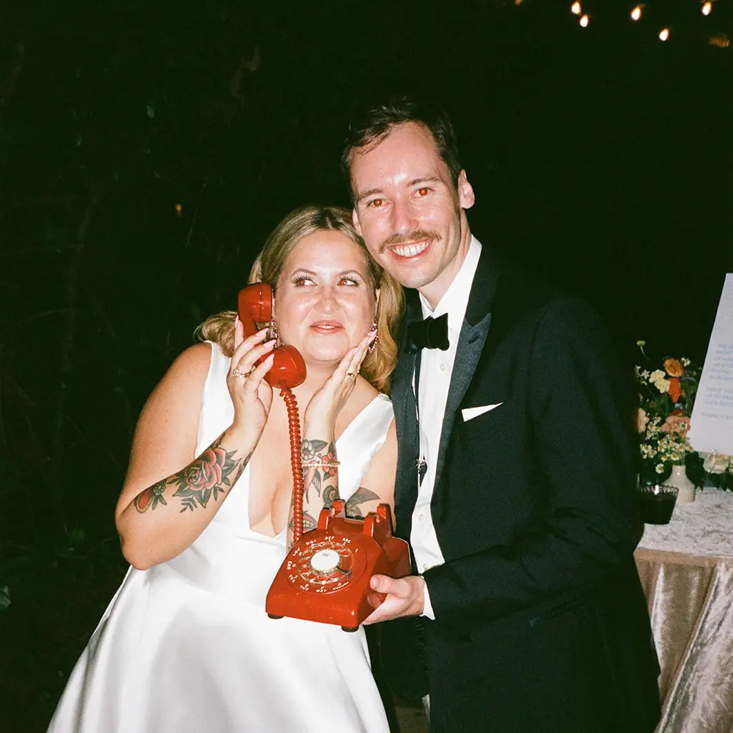Man and woman in formal attire with a red rotary phone at an event.