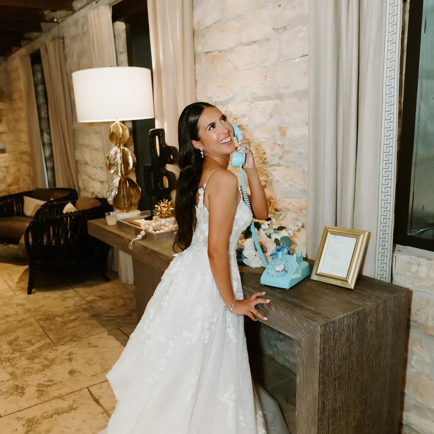 Woman in a white dress holding a blue vintage phone in an elegant room.