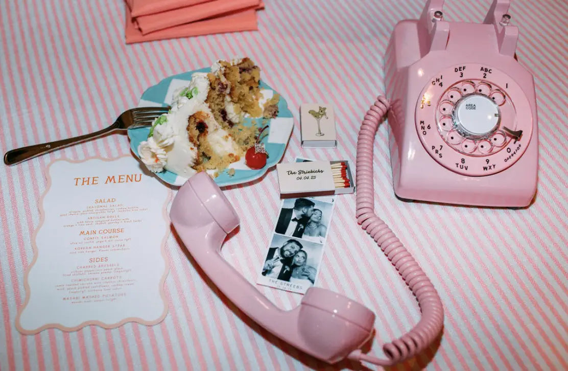 a pink rotary phone on a pink table next to cake and a box of matches