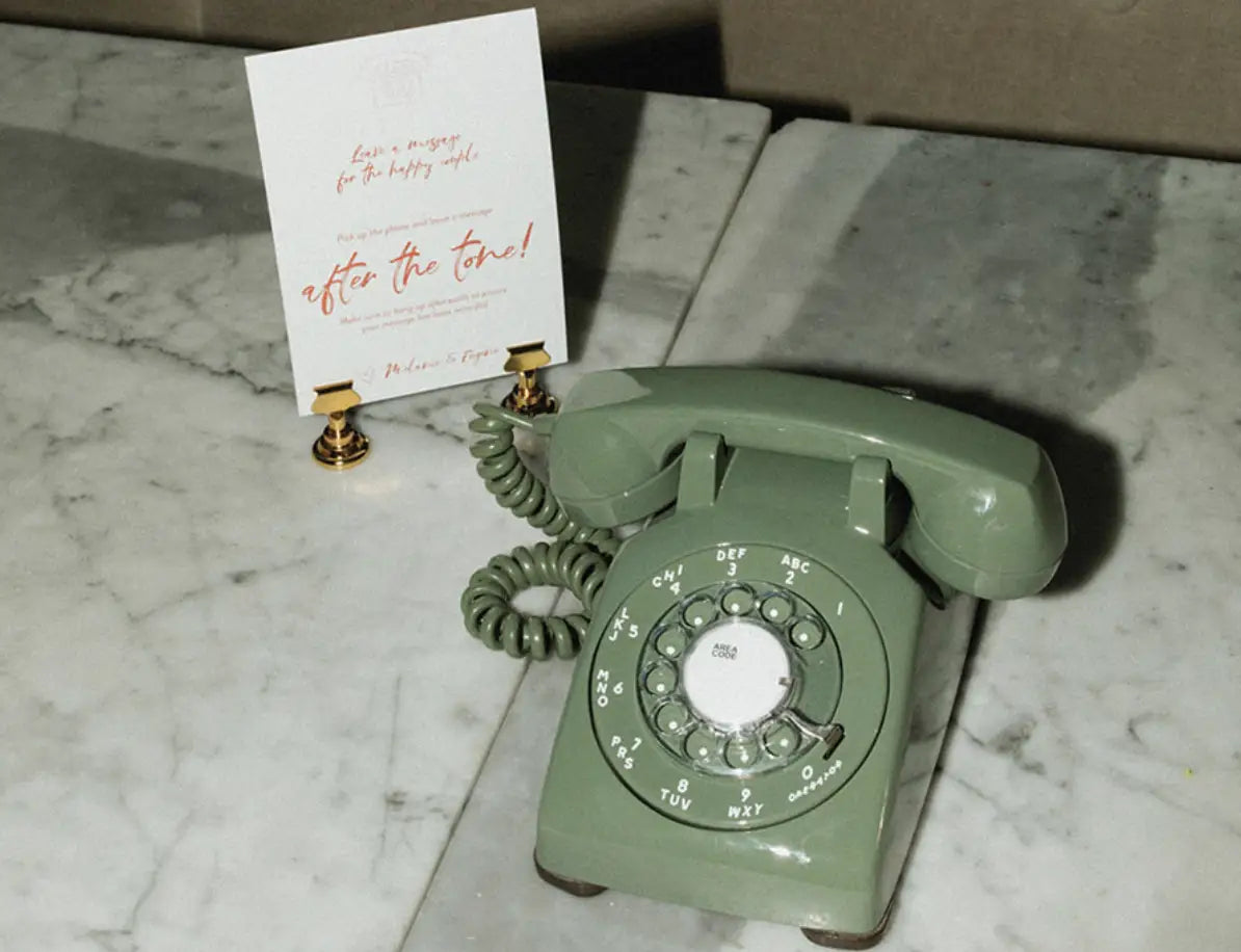 a green rotary phone on a marble table next to a paper sign