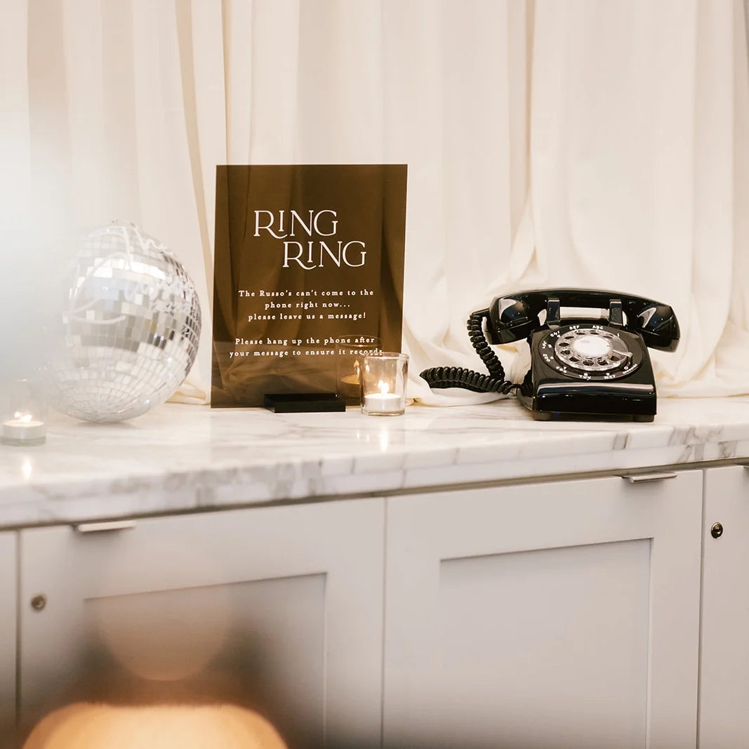 Vintage black rotary phone on a marble surface with a Ring Ring sign.