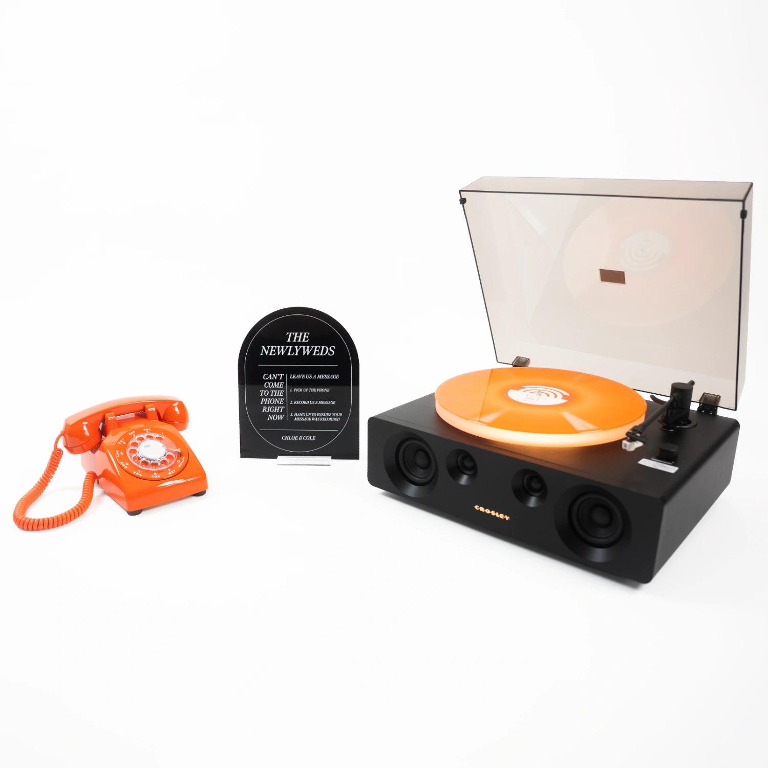 The Bowie bundle: an orange rotary phone audio guestbook, a black Icon acrylic sign reading The Newlyweds, and a record player spinning a custom vinyl record.