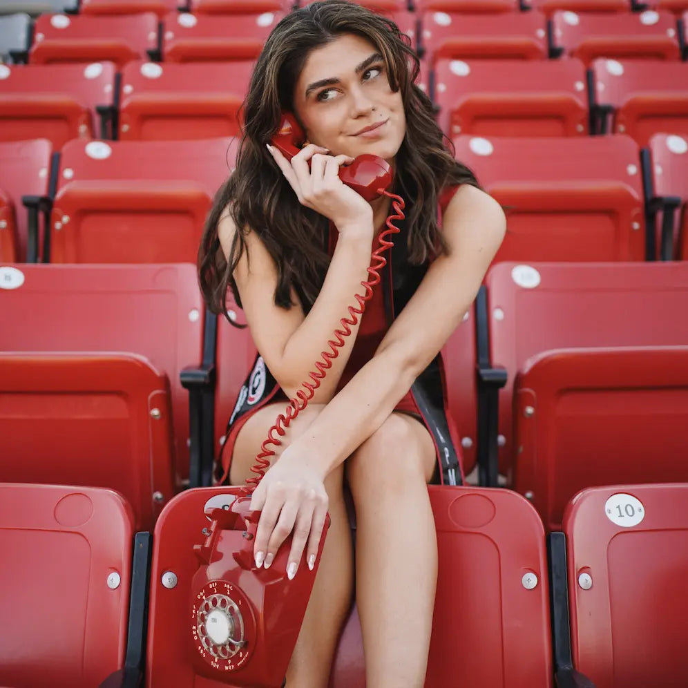 Woman sitting in a stadium with a red vintage phone, surrounded by red seats.