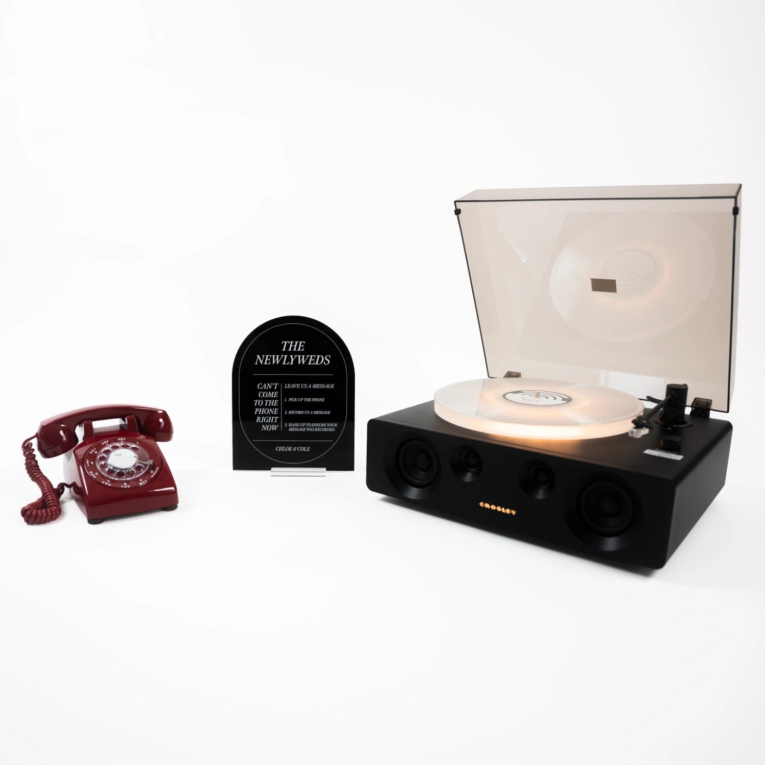 The Stevie bundle: a red rotary phone audio guestbook, a black Icon acrylic sign reading The Newlyweds, and a record player spinning a custom vinyl record.