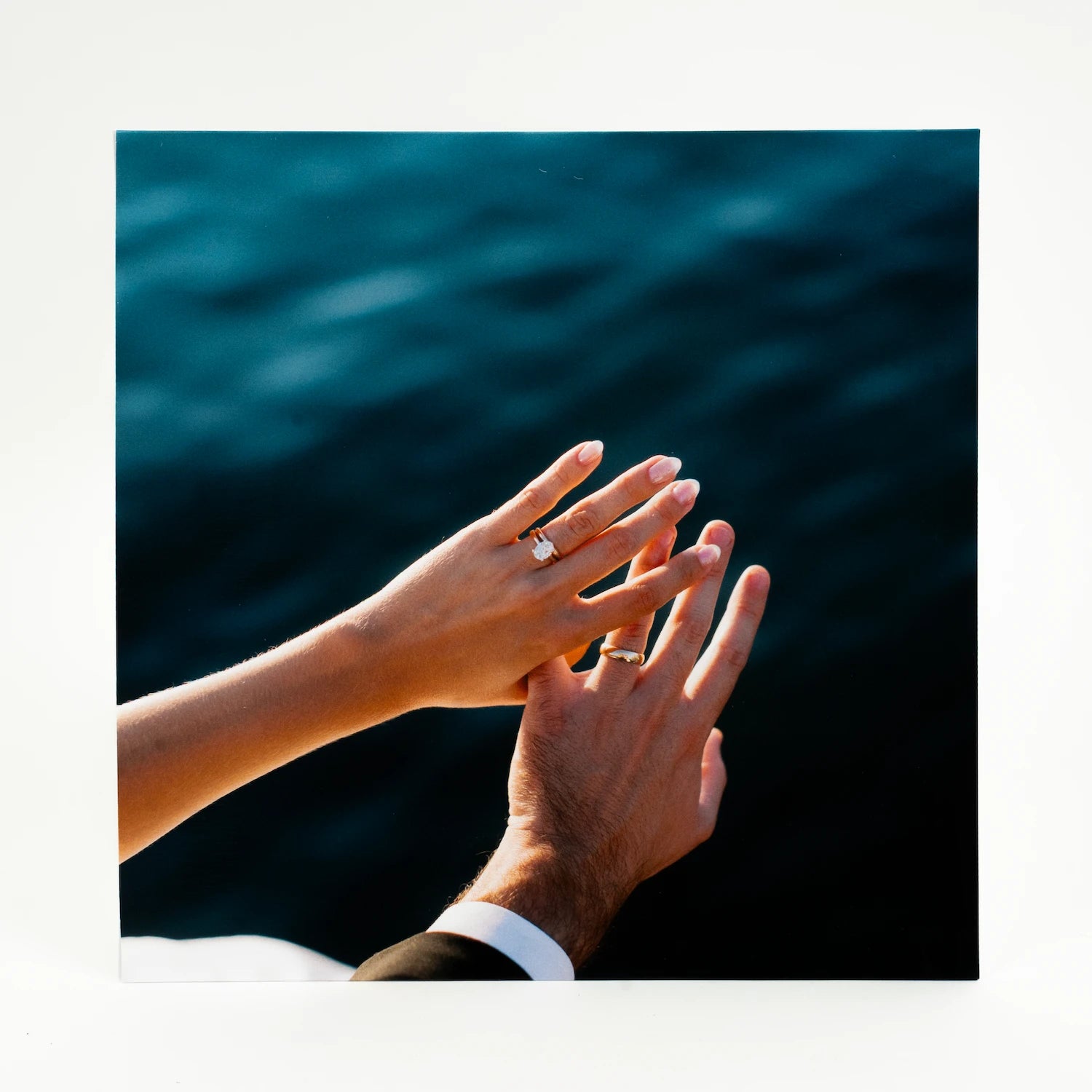 Two hands with rings held together in front of a body of water