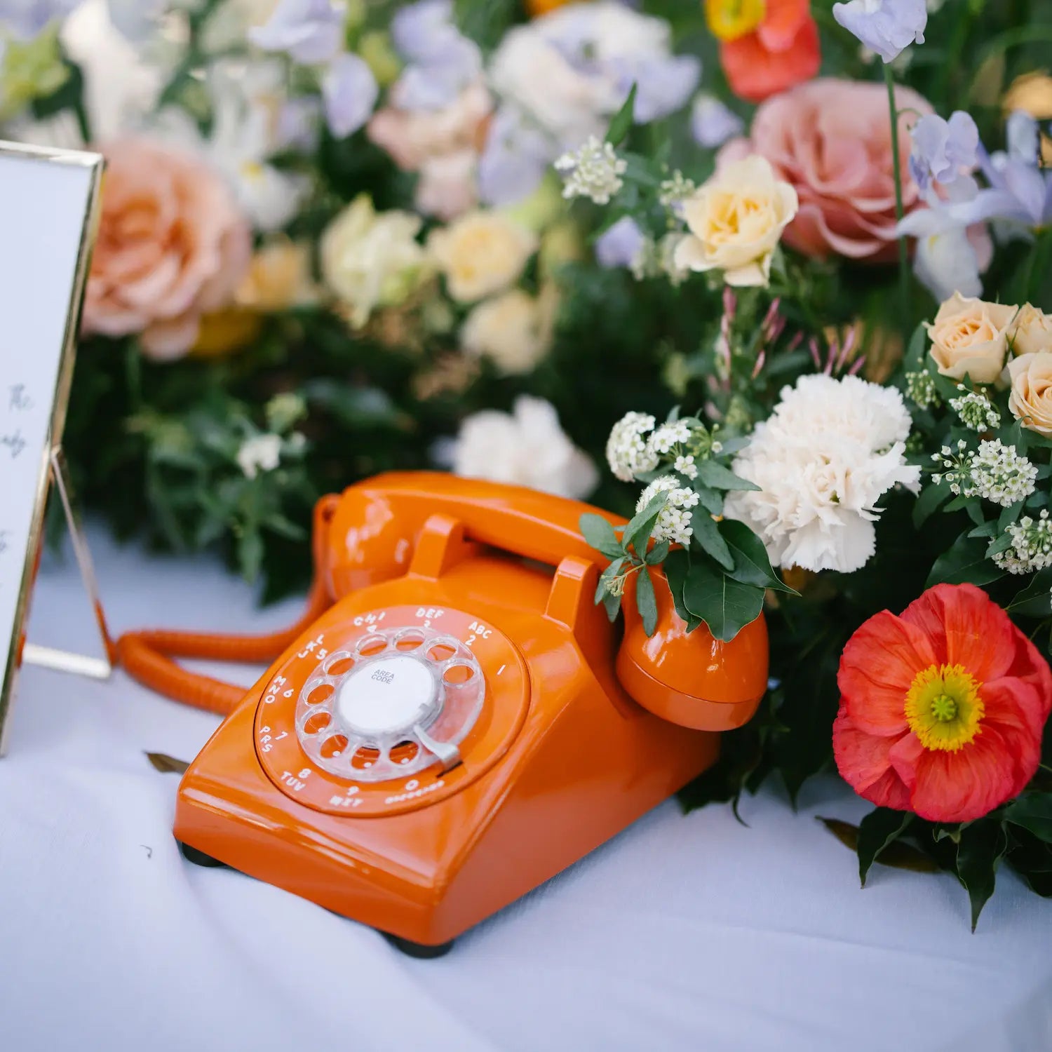 Vintage orange rotary phone surrounded by colorful flowers on a table.
