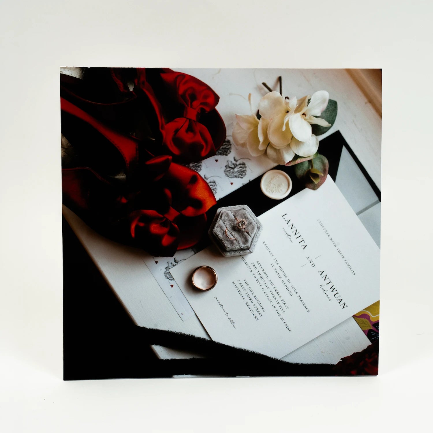 Wedding invitation with red flowers and rings on a white surface